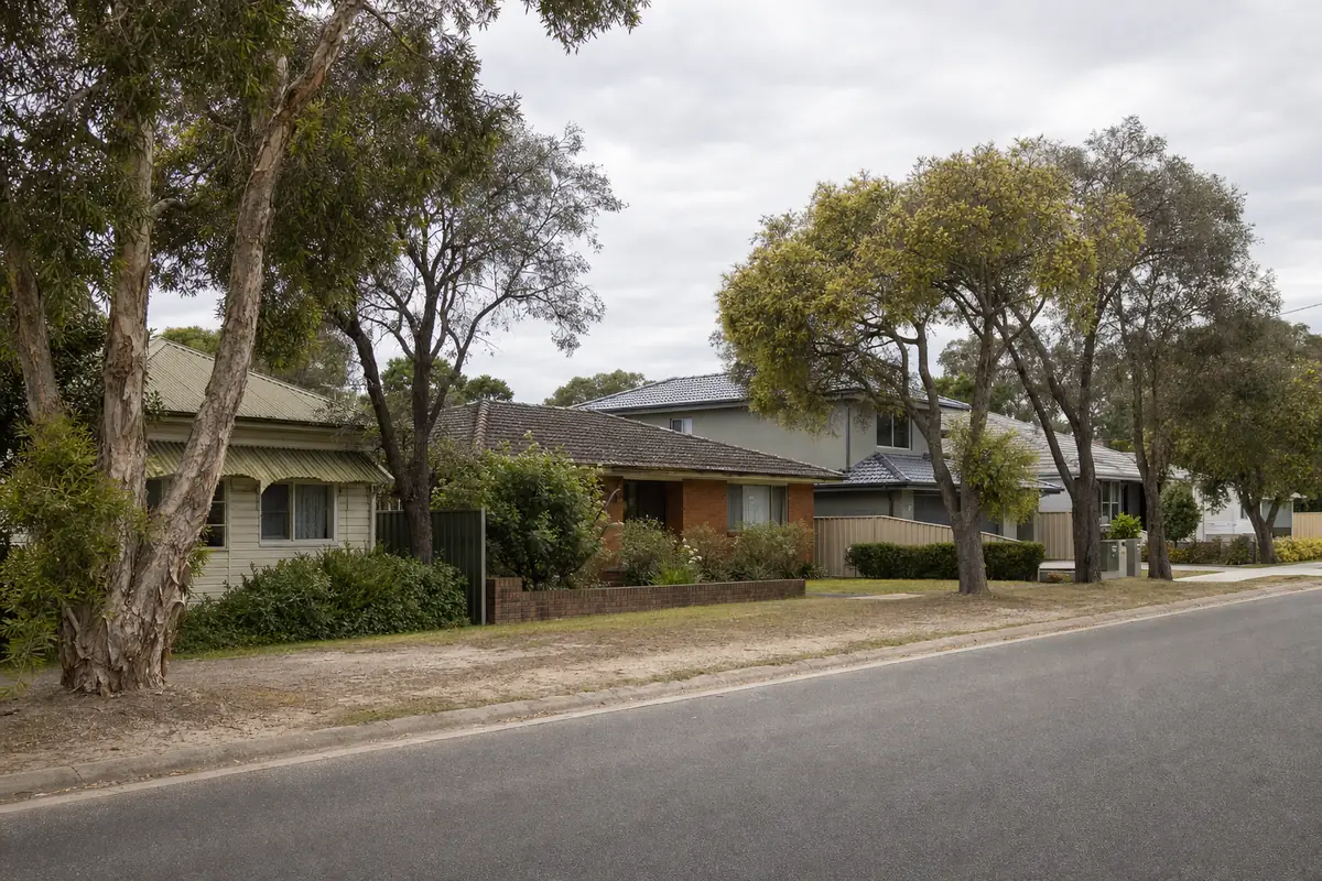 A quiet Central Coast street with a weatherboard cottage, a brick-veneer house and a newer rendered home side by side under paperbark and wattle — pressure cleaning, Central Coast. Illustrative example.